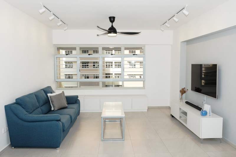 Living room with a blue fabric sofa, low white window cabinets, a white TV console and a ceiling fan - HDB flat renovation with a navy kitchen and a glass-walled walk-in wardrobe (407B) | Larry Contractors, HDB Licensed Renovation Contractor, Singapore