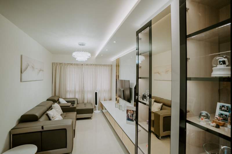 Living room with a brown leather sofa, long floating TV console and a black-framed glass display cabinet - HDB flat renovation in cream and mirror-trim laminate with a galley kitchen (C10) | Larry Contractors, HDB Licensed Renovation Contractor, Singapore