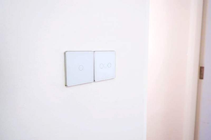 Two white touch-panel light switches on a plain white wall - HDB flat renovation in white shaker-style carpentry with brass handles (C05) | Larry Contractors, HDB Licensed Renovation Contractor, Singapore