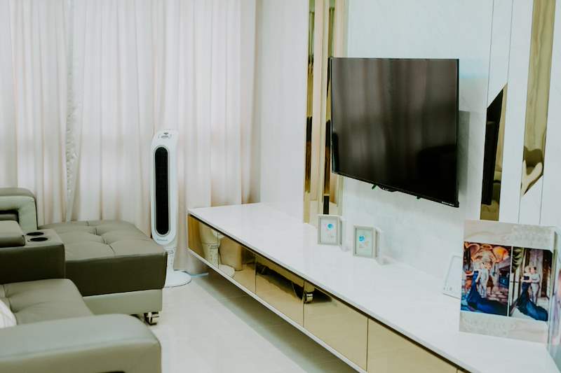Wall-mounted TV on a cream laminate wall with gold mirror strips above the floating console - HDB flat renovation in cream and mirror-trim laminate with a galley kitchen (C10) | Larry Contractors, HDB Licensed Renovation Contractor, Singapore