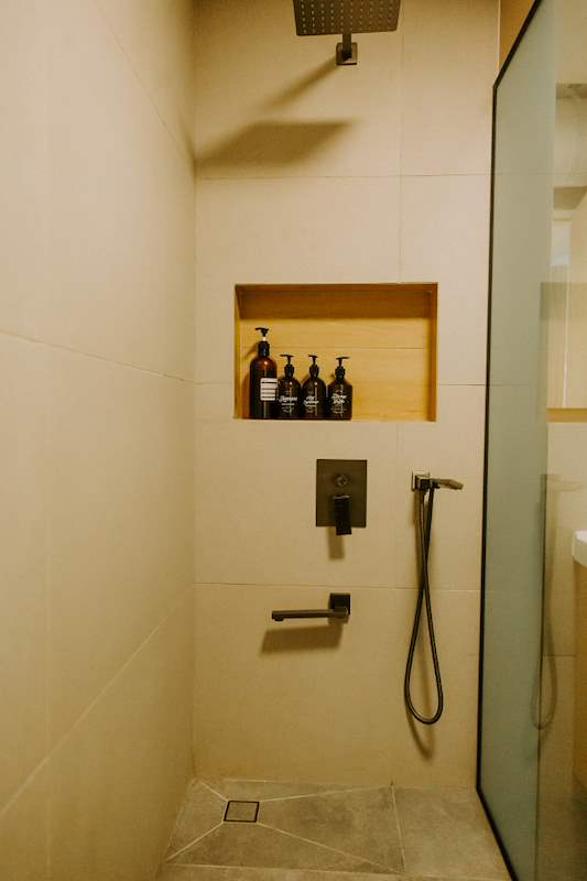 Shower with a rain head, black mixer and a timber-lined shelf niche - Full HDB maisonette renovation with a curved timber-slat island and lit staircase (140BB) | Larry Contractors, HDB Licensed Renovation Contractor, Singapore