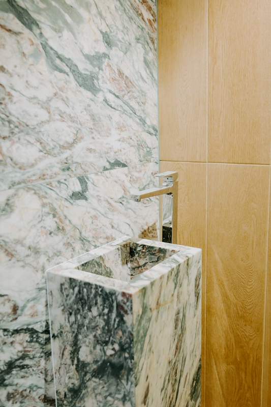 Green-veined marble basin and wall panel beside oak-look panelling in the powder room - Condo apartment renovation with a limestone feature wall and dark green kitchen (38MR) | Larry Contractors, HDB Licensed Renovation Contractor, Singapore