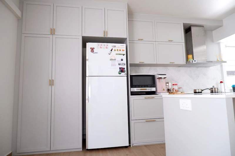 White shaker-style kitchen with tall cabinets around the fridge, a cooker hood and a marble-look splashback - HDB flat renovation in white shaker-style carpentry with brass handles (C05) | Larry Contractors, HDB Licensed Renovation Contractor, Singapore