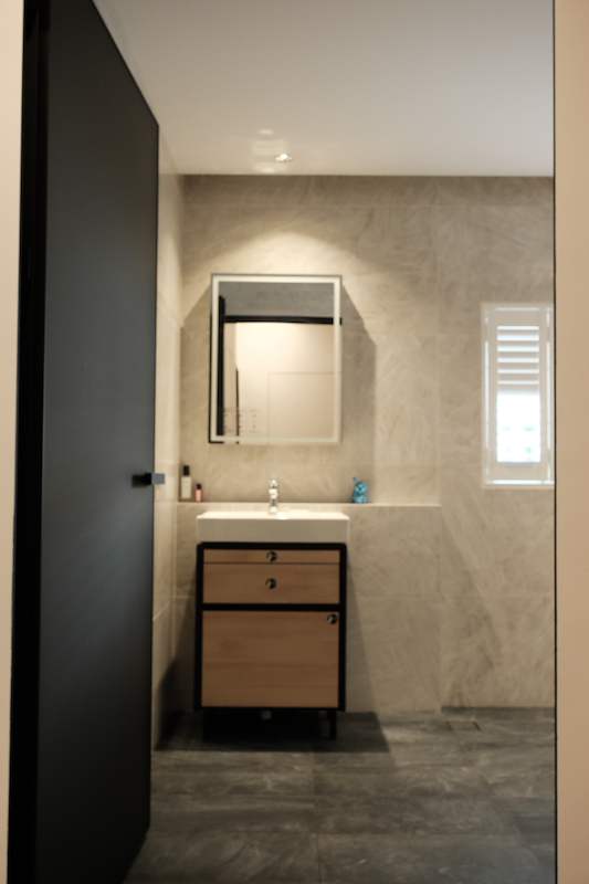 Bathroom vanity with a timber-front drawer unit, mirror cabinet and grey wall tiles, seen through a dark doorway - Terrace house renovation with new facade and full interior (3TBA) | Larry Contractors, HDB Licensed Renovation Contractor, Singapore