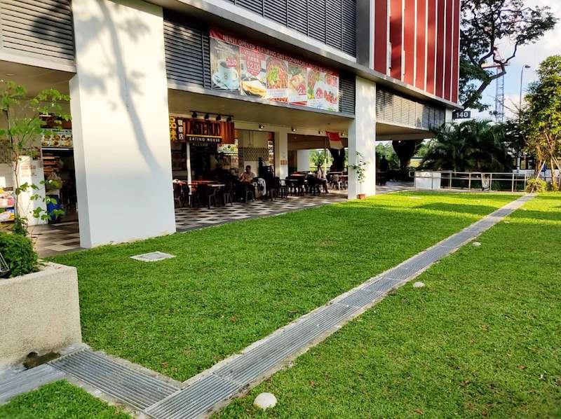 Before: the coffee shop under the block with an open lawn where the extension now stands - Covered dining extension for a coffee shop under an HDB block (140CD) | Larry Contractors, HDB Licensed Renovation Contractor, Singapore