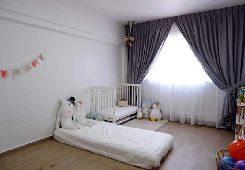 Nursery with a white cot, a floor mattress, grey curtains and a bunting on the wall - HDB flat renovation in white shaker-style carpentry with brass handles (C05) | Larry Contractors, HDB Licensed Renovation Contractor, Singapore