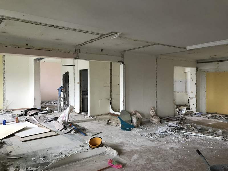 During demolition: the flat stripped to bare walls with rubble, exposed pipes and hacked openings - HDB flat renovation with full-height carpentry and a wood-tone kitchen (C12) | Larry Contractors, HDB Licensed Renovation Contractor, Singapore