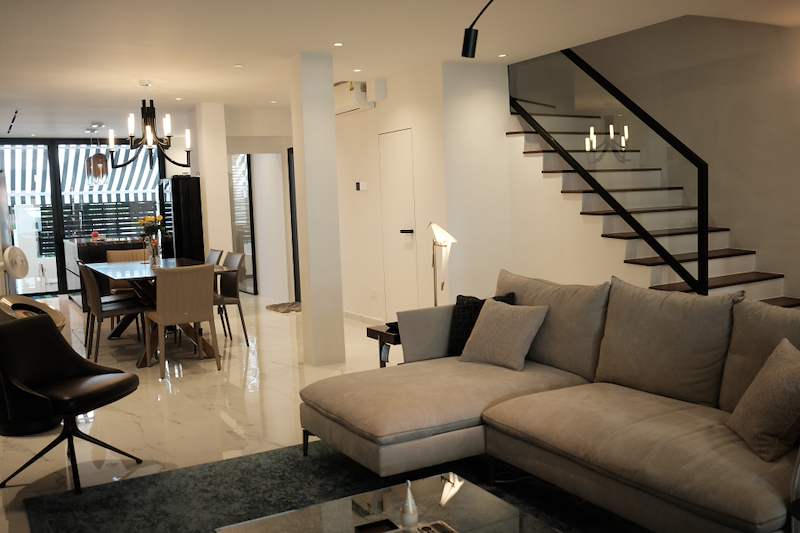 Open-plan living and dining area with a beige sectional sofa, a dining table and a black metal staircase with timber treads - Terrace house renovation with new facade and full interior (3TBA) | Larry Contractors, HDB Licensed Renovation Contractor, Singapore