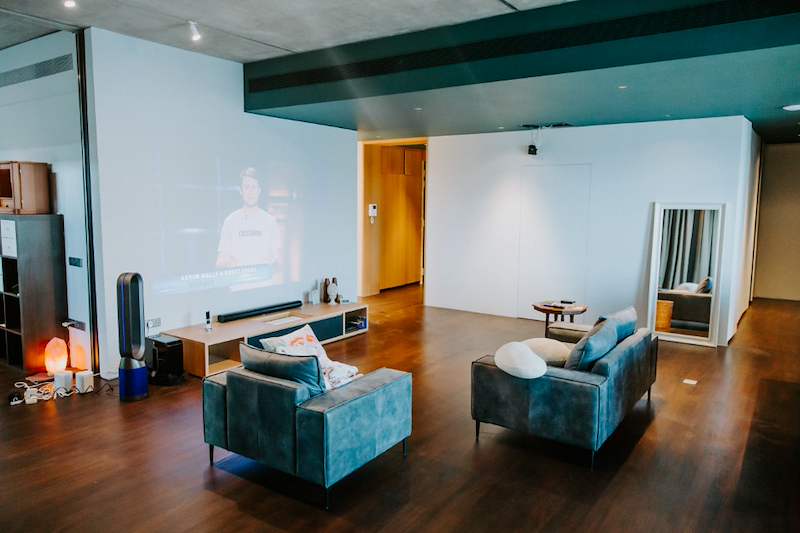 After: living room with two teal armchairs, dark timber flooring, a low TV console and a teal ceiling bulkhead - Condo apartment renovation with a limestone feature wall and dark green kitchen (38MR) | Larry Contractors, HDB Licensed Renovation Contractor, Singapore