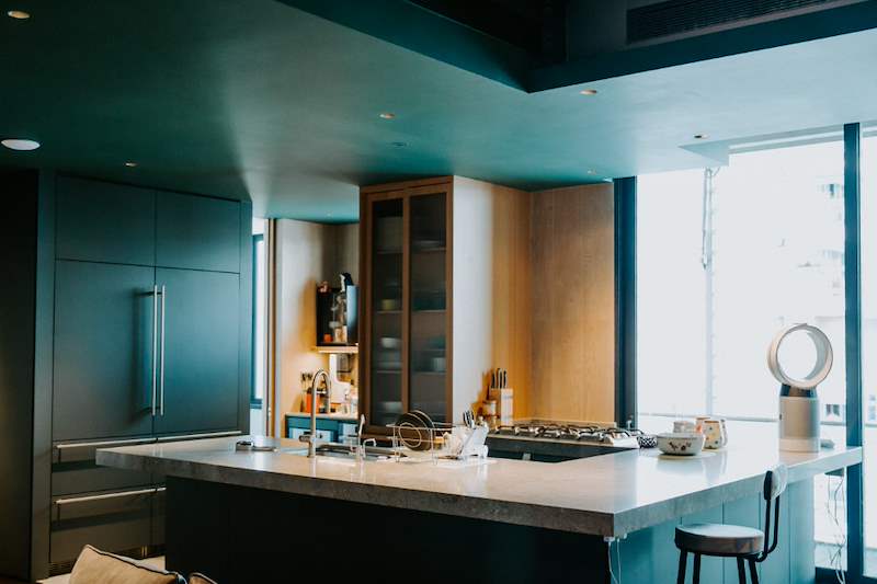 Dark green kitchen with a stone island, bar stools and full-height windows beyond - Condo apartment renovation with a limestone feature wall and dark green kitchen (38MR) | Larry Contractors, HDB Licensed Renovation Contractor, Singapore