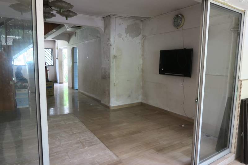 Before: the living room with stained walls, an old wall-mounted TV and a glass sliding door to the balcony - HDB flat renovation with a new kitchen, false ceiling and repaired cladding (320WS) | Larry Contractors, HDB Licensed Renovation Contractor, Singapore