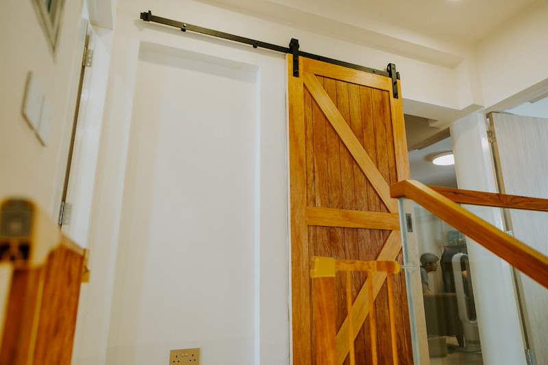 Timber sliding barn door on a black track at the top of the stairs - Full HDB maisonette renovation with a curved timber-slat island and lit staircase (140BB) | Larry Contractors, HDB Licensed Renovation Contractor, Singapore