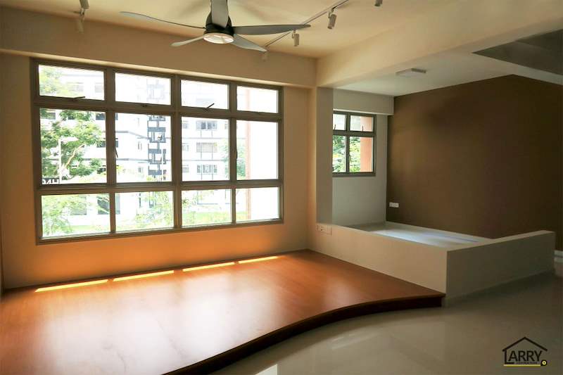 After: the curved timber-laminate platform under the living room windows with the brown feature wall beyond - HDB flat renovation with a platform bay window seat and blue kitchen (C20) | Larry Contractors, HDB Licensed Renovation Contractor, Singapore