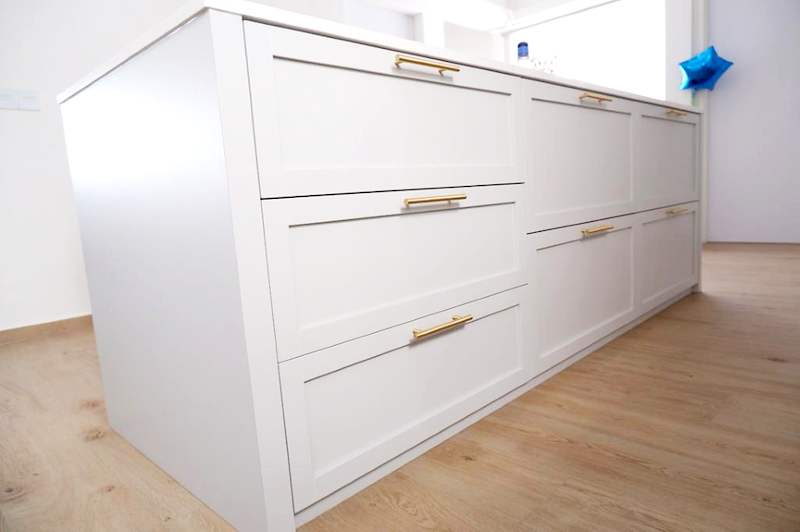 White shaker-style drawer unit with brass handles on a light timber-look floor - HDB flat renovation in white shaker-style carpentry with brass handles (C05) | Larry Contractors, HDB Licensed Renovation Contractor, Singapore