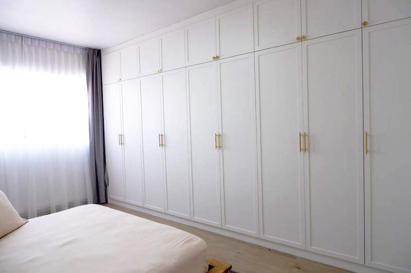 Bedroom with a wall of white shaker-style wardrobes with brass handles beside the window - HDB flat renovation in white shaker-style carpentry with brass handles (C05) | Larry Contractors, HDB Licensed Renovation Contractor, Singapore