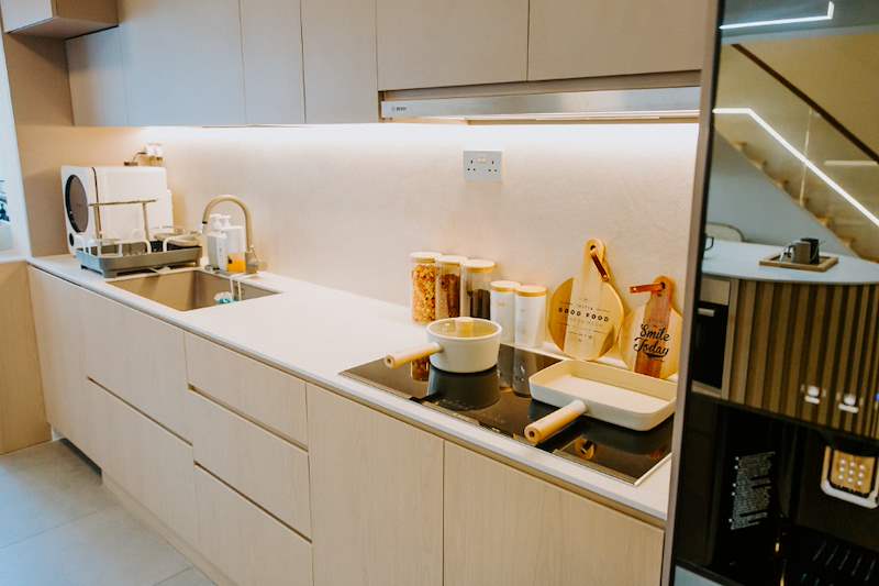 Kitchen run with beige cabinets, a white worktop, induction hob and a backlit splashback - Full HDB maisonette renovation with a curved timber-slat island and lit staircase (140BB) | Larry Contractors, HDB Licensed Renovation Contractor, Singapore