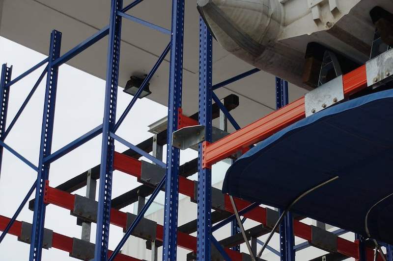 Looking up at the blue upright frames, orange beams and galvanised brackets that carry a boat hull - Heavy-duty storage racking for boats and jet skis (Sentosa) | Larry Contractors, HDB Licensed Renovation Contractor, Singapore