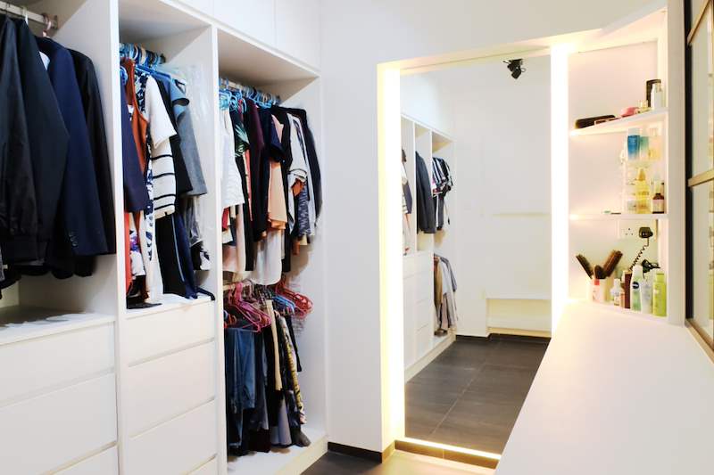 Walk-in wardrobe with open hanging rails, white drawers and lit shelving behind a black-framed glass wall - HDB flat renovation with a navy kitchen and a glass-walled walk-in wardrobe (407B) | Larry Contractors, HDB Licensed Renovation Contractor, Singapore