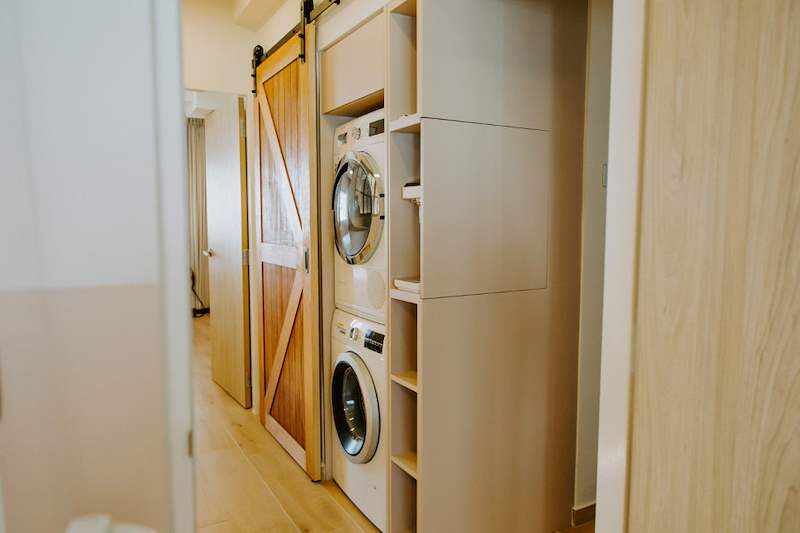 Laundry cupboard with a stacked washer and dryer beside the barn door - Full HDB maisonette renovation with a curved timber-slat island and lit staircase (140BB) | Larry Contractors, HDB Licensed Renovation Contractor, Singapore