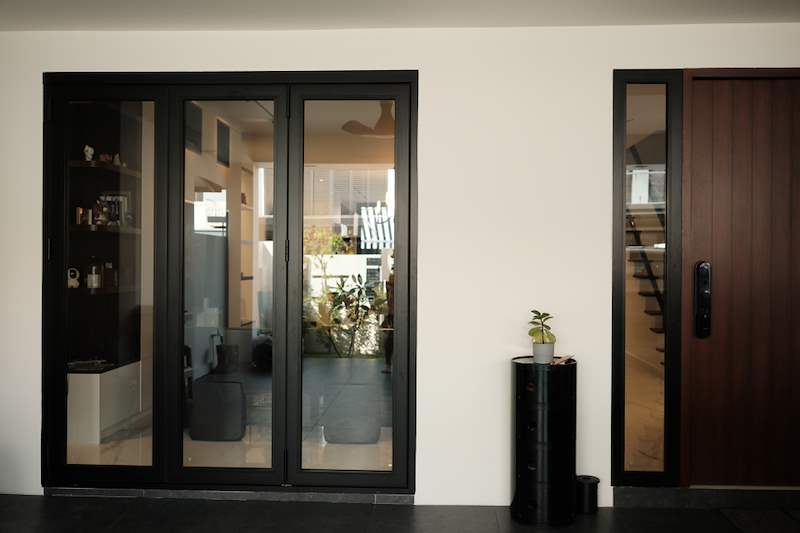 Black-framed glass folding doors opening onto the porch, next to the timber front door - Terrace house renovation with new facade and full interior (3TBA) | Larry Contractors, HDB Licensed Renovation Contractor, Singapore