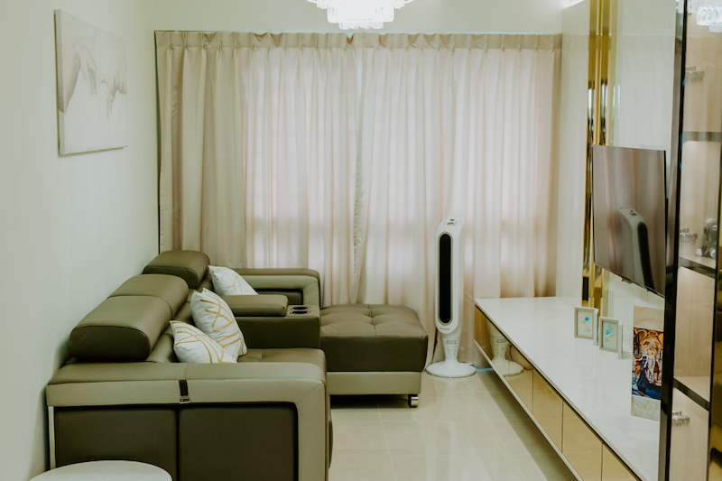 Living room with a leather sofa, sheer curtains, floating TV console and a mirror-strip feature wall - HDB flat renovation in cream and mirror-trim laminate with a galley kitchen (C10) | Larry Contractors, HDB Licensed Renovation Contractor, Singapore