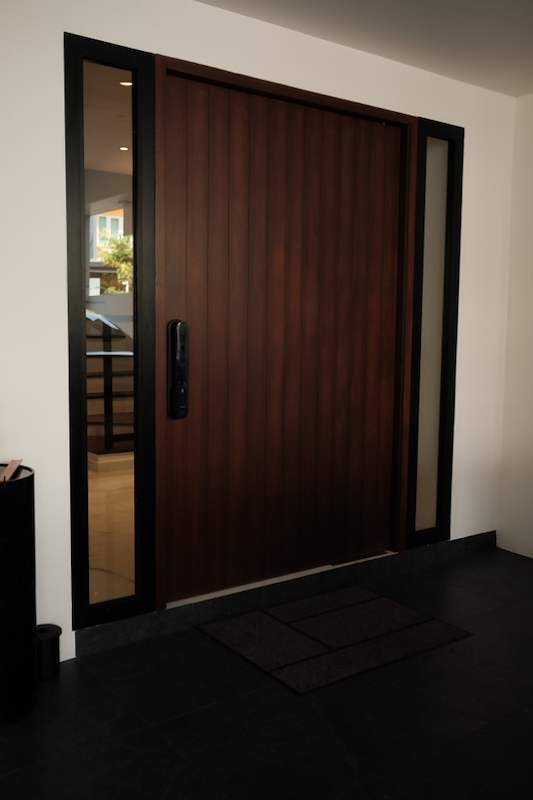 The timber pivot front door closed, flanked by glass side panels, with a dark tiled floor at the entrance - Terrace house renovation with new facade and full interior (3TBA) | Larry Contractors, HDB Licensed Renovation Contractor, Singapore