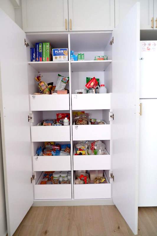 Tall pantry cabinet opened to show pull-out drawer shelves stocked with groceries - HDB flat renovation in white shaker-style carpentry with brass handles (C05) | Larry Contractors, HDB Licensed Renovation Contractor, Singapore