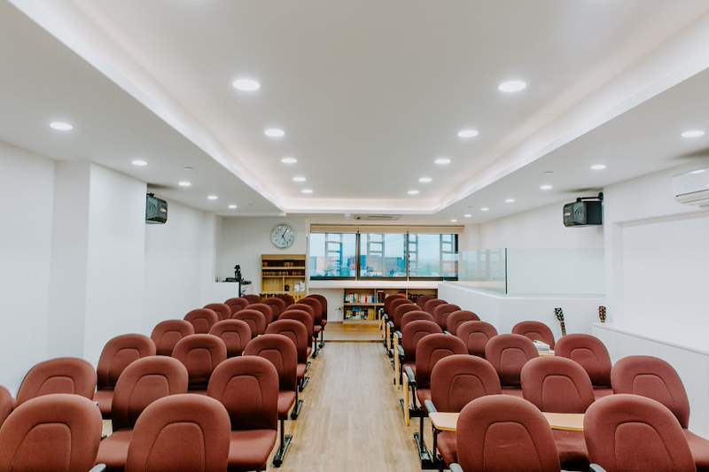 Church hall looking towards the rear, rows of maroon chairs, wall speakers and a glass-railed balcony - Church hall fit-out with a timber stage and custom podium (62JBCC) | Larry Contractors, HDB Licensed Renovation Contractor, Singapore