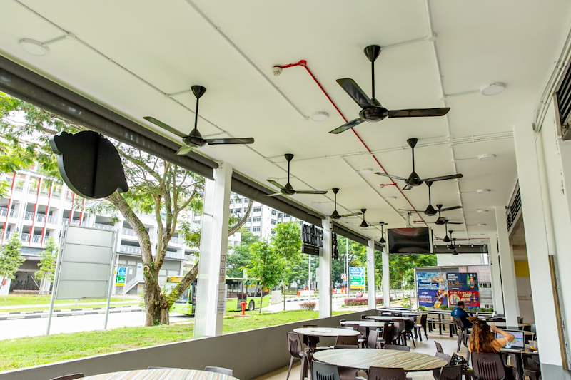 Inside the extension: ceiling fans under the new roof, dining tables and the view to the road - Covered dining extension for a coffee shop under an HDB block (140CD) | Larry Contractors, HDB Licensed Renovation Contractor, Singapore