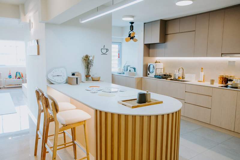 Curved timber-slat kitchen island with bar stools and the beige kitchen behind - Full HDB maisonette renovation with a curved timber-slat island and lit staircase (140BB) | Larry Contractors, HDB Licensed Renovation Contractor, Singapore