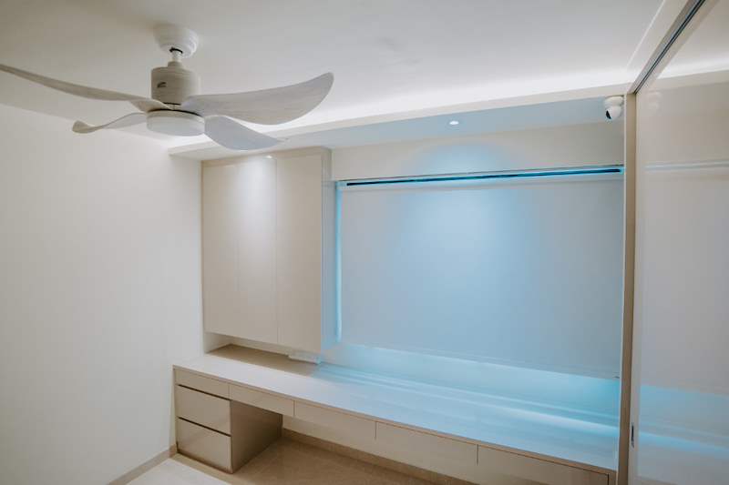 Bedroom with a ceiling fan, built-in desk and drawers under the window and cove lighting - HDB flat renovation in cream and mirror-trim laminate with a galley kitchen (C10) | Larry Contractors, HDB Licensed Renovation Contractor, Singapore