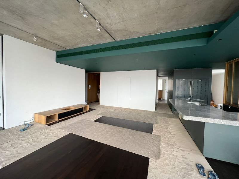 Before: the open-plan living area with a bare concrete ceiling and floor protection down - Condo apartment renovation with a limestone feature wall and dark green kitchen (38MR) | Larry Contractors, HDB Licensed Renovation Contractor, Singapore