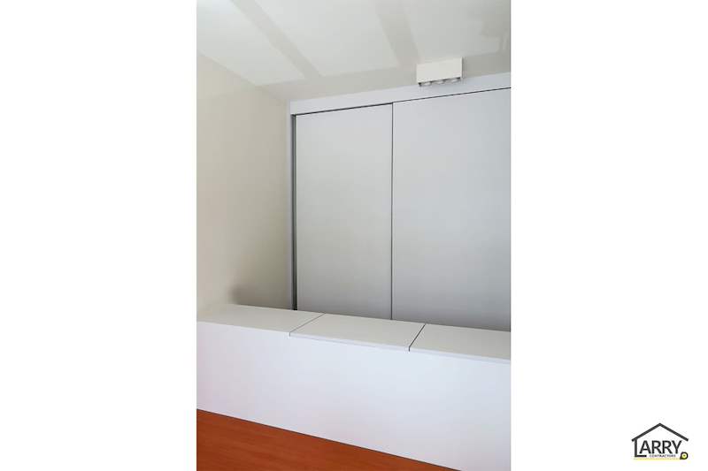 Grey sliding wardrobe doors and a white storage bench beside the timber-laminate platform - HDB flat renovation with a platform bay window seat and blue kitchen (C20) | Larry Contractors, HDB Licensed Renovation Contractor, Singapore