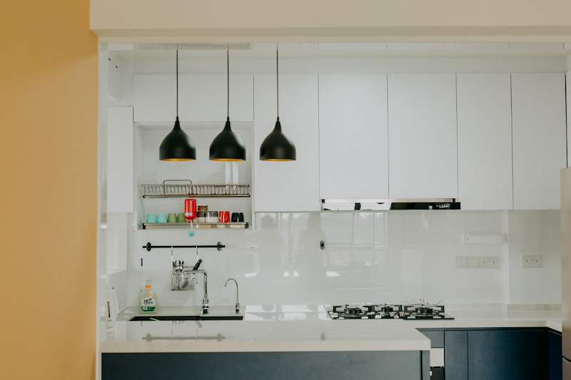Kitchen counter with a sink, dish rack, cooker hood and three black pendant lights - HDB flat renovation with a glass-partitioned study, hidden shoe cabinet and navy kitchen (442BB) | Larry Contractors, HDB Licensed Renovation Contractor, Singapore