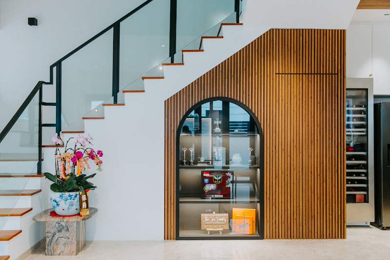 After: close view of the arched glass display cabinet set into the timber-slat wall beneath the stairs, wine fridge alongside - Landed house renovation with new facade, staircase and interiors (39EW) | Larry Contractors, HDB Licensed Renovation Contractor, Singapore