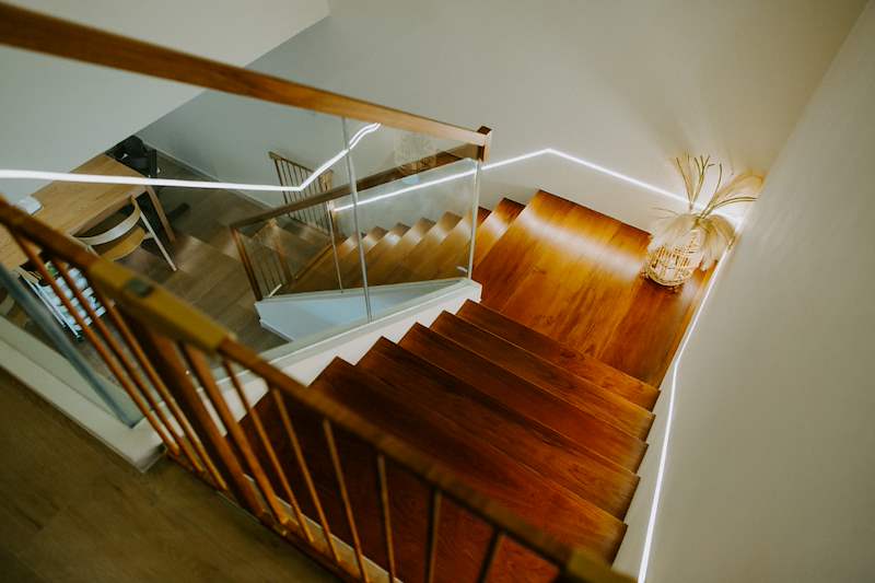 Timber staircase with a glass balustrade and timber handrail seen from above - Full HDB maisonette renovation with a curved timber-slat island and lit staircase (140BB) | Larry Contractors, HDB Licensed Renovation Contractor, Singapore