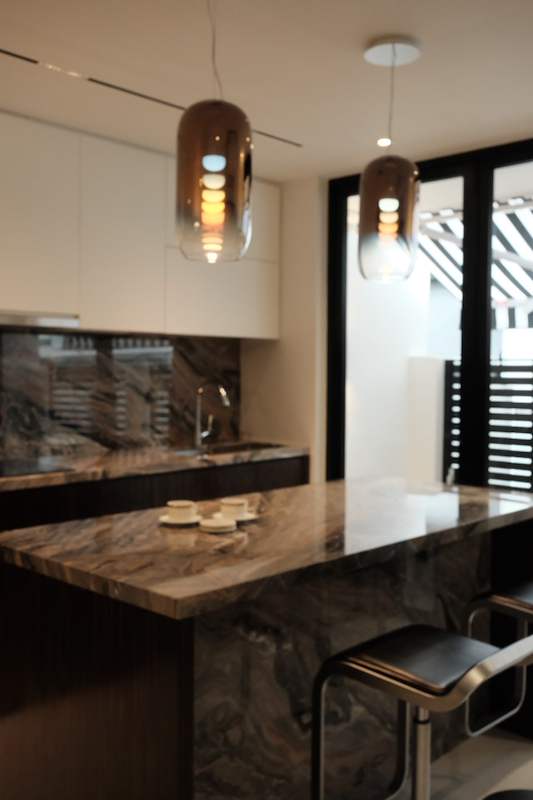 Kitchen island with a veined stone top, a dark base and two bar stools, pendant lights above and the balcony beyond - Terrace house renovation with new facade and full interior (3TBA) | Larry Contractors, HDB Licensed Renovation Contractor, Singapore