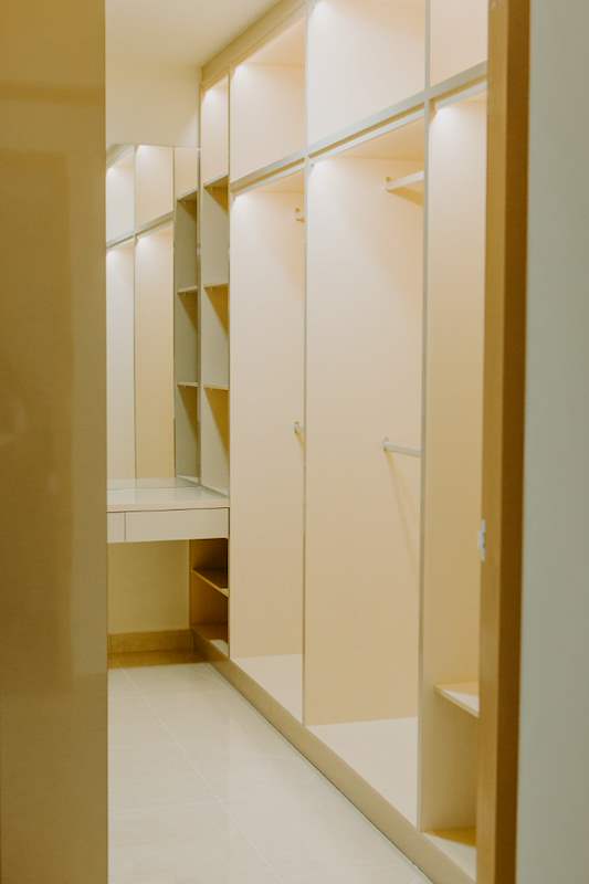 Walk-in wardrobe with lit open shelving, hanging rails and drawers in cream laminate - HDB flat renovation in cream and mirror-trim laminate with a galley kitchen (C10) | Larry Contractors, HDB Licensed Renovation Contractor, Singapore