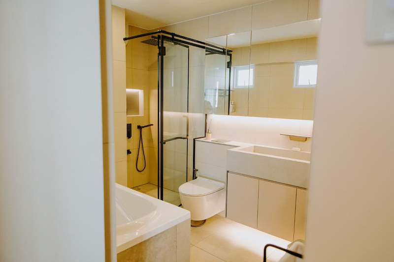 Bathroom with a black-framed shower screen, built-in tub, wall-hung toilet and a lit vanity - Full HDB maisonette renovation with a curved timber-slat island and lit staircase (140BB) | Larry Contractors, HDB Licensed Renovation Contractor, Singapore