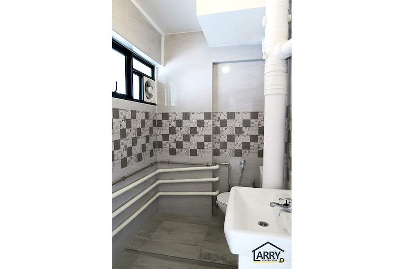 Bathroom with a white basin, toilet, patterned tile band and pipework painted white - HDB resale flat renovation with polished terrazzo floors, new kitchen and bathrooms (C04) | Larry Contractors, HDB Licensed Renovation Contractor, Singapore