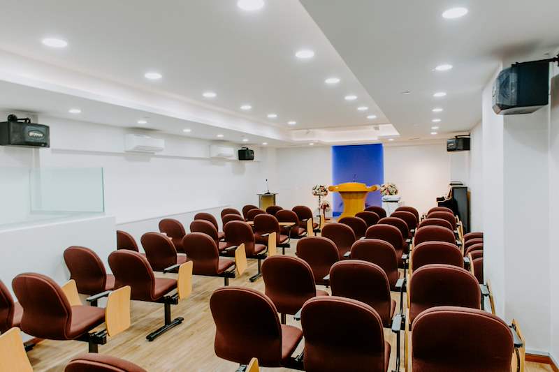 Church hall with rows of maroon upholstered chairs, a coffered ceiling with recessed lights and a stage at the front - Church hall fit-out with a timber stage and custom podium (62JBCC) | Larry Contractors, HDB Licensed Renovation Contractor, Singapore