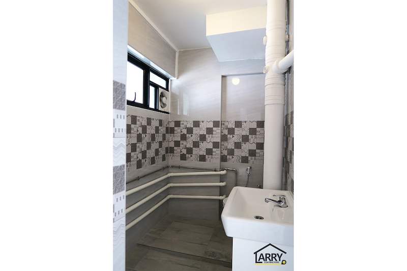 Bathroom with a white basin, toilet, patterned tile band and pipework painted white - HDB resale flat renovation with polished terrazzo floors, new kitchen and bathrooms (C04) | Larry Contractors, HDB Licensed Renovation Contractor, Singapore