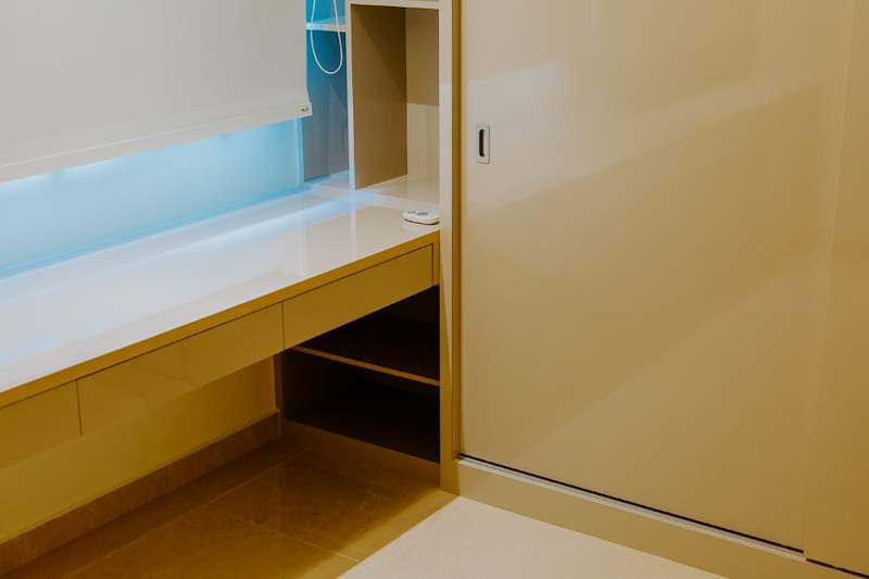 Built-in desk beside a sliding wardrobe door with backlit overhead storage - HDB flat renovation in cream and mirror-trim laminate with a galley kitchen (C10) | Larry Contractors, HDB Licensed Renovation Contractor, Singapore