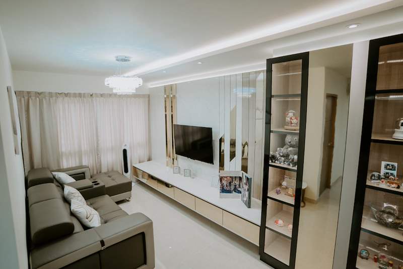 Living room looking towards the window, floating TV console and glass display cabinet on the right - HDB flat renovation in cream and mirror-trim laminate with a galley kitchen (C10) | Larry Contractors, HDB Licensed Renovation Contractor, Singapore
