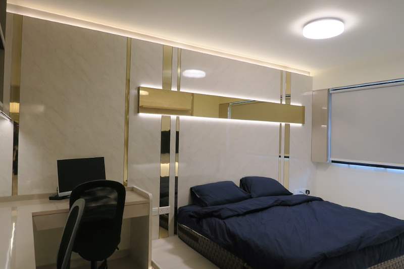 Bedroom with a blue-covered bed, a computer desk and cream laminate panels with mirror strips - HDB flat renovation in cream and mirror-trim laminate with a galley kitchen (C10) | Larry Contractors, HDB Licensed Renovation Contractor, Singapore