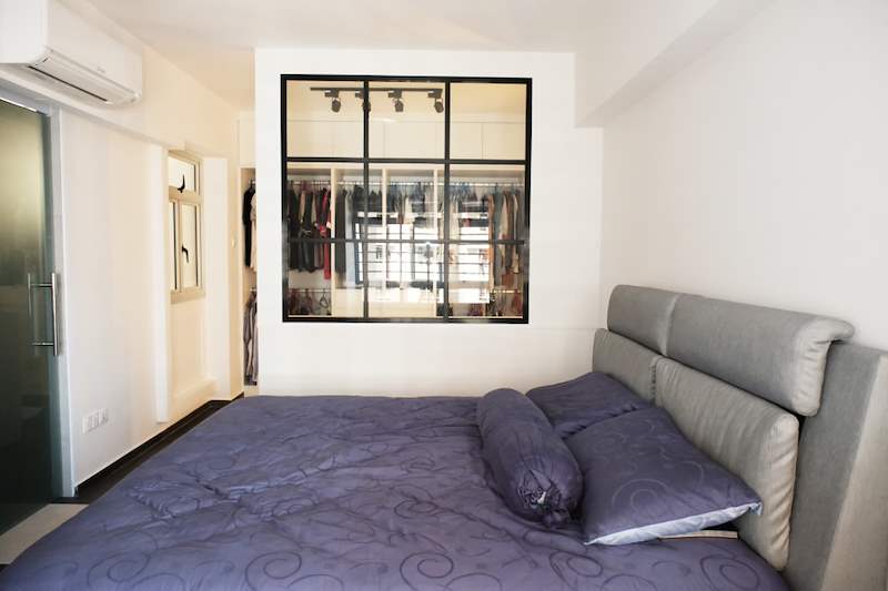 Bedroom with a grey upholstered bed and a black-framed glass wall to the lit walk-in wardrobe - HDB flat renovation with a navy kitchen and a glass-walled walk-in wardrobe (407B) | Larry Contractors, HDB Licensed Renovation Contractor, Singapore