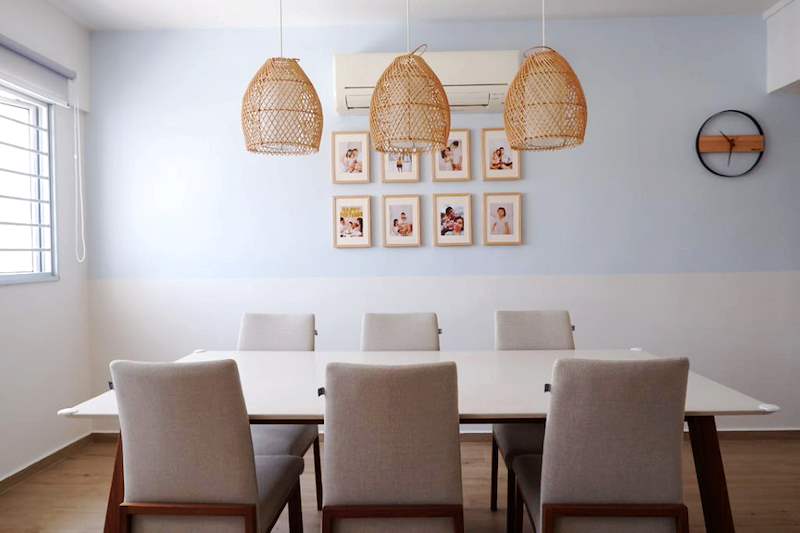 Dining table with beige upholstered chairs under three rattan pendant lights, family photos on the wall - HDB flat renovation in white shaker-style carpentry with brass handles (C05) | Larry Contractors, HDB Licensed Renovation Contractor, Singapore