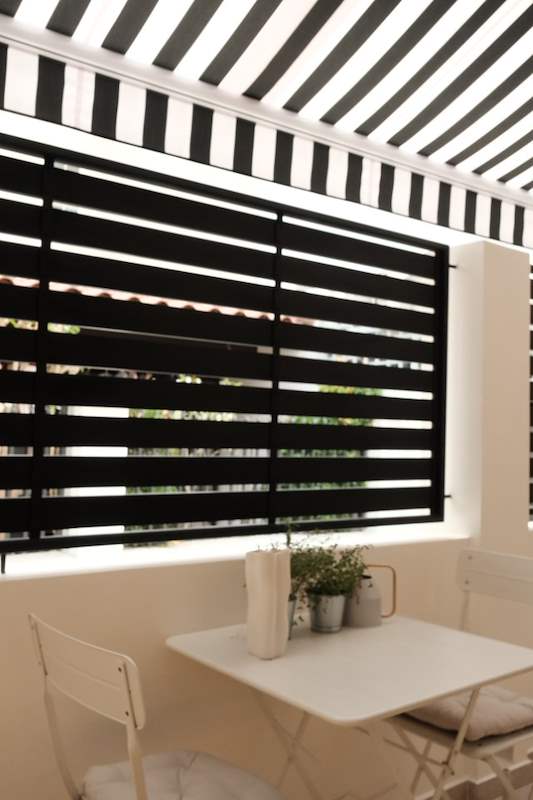 Balcony corner with a striped awning, a black slatted screen and a small white bistro table and chair - Terrace house renovation with new facade and full interior (3TBA) | Larry Contractors, HDB Licensed Renovation Contractor, Singapore