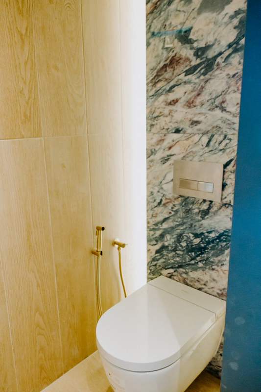 Powder room with a wall-hung toilet, green marble wall panel and oak-look panelling - Condo apartment renovation with a limestone feature wall and dark green kitchen (38MR) | Larry Contractors, HDB Licensed Renovation Contractor, Singapore