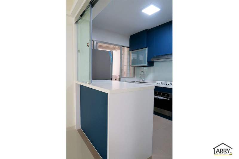 Kitchen with blue lower cabinets, a white worktop, a built-in oven and a white peninsula counter - HDB flat renovation with a platform bay window seat and blue kitchen (C20) | Larry Contractors, HDB Licensed Renovation Contractor, Singapore